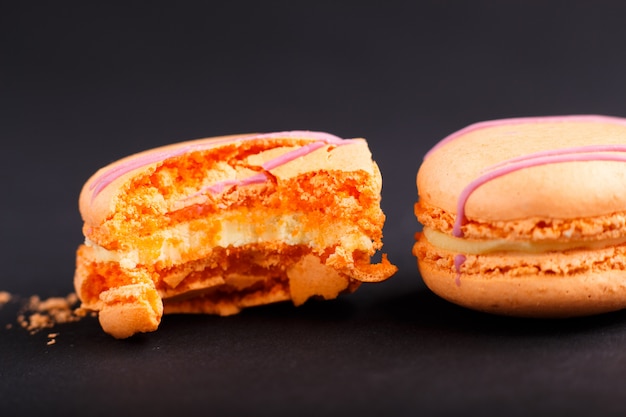 Macarons ou macarons orange entiers et mordus sur fond noir