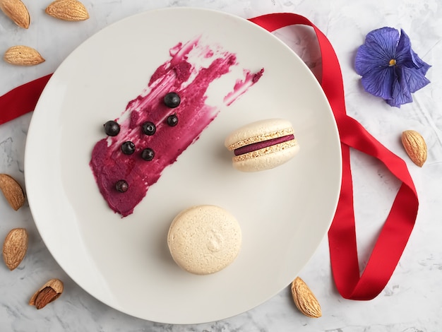 Macarons maison avec garniture de groseille sur une plaque grise. Amandes, baies de cassis et garniture pour biscuits sur une assiette. Mise à plat.