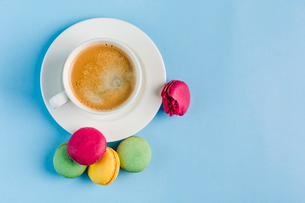 Macarons multicolores avec une tasse de café blanche sur un fond bleu, vue de dessus, plat poser avec fond