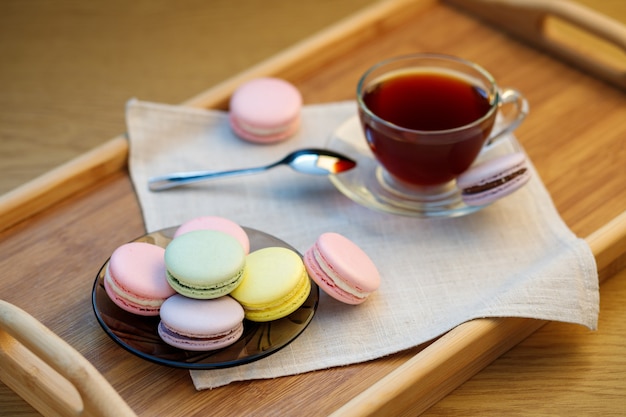 Photo macarons multicolores et une tasse de thé sur un plateau en bois thé du matin et bonbons