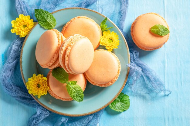 Photo macarons orange savoureux et frais avec des fleurs sur table bleue