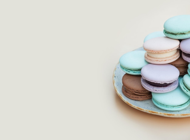 Macarons de pâtisserie de différentes couleurs pastel dans une assiette sur fond beige avec espace de copie