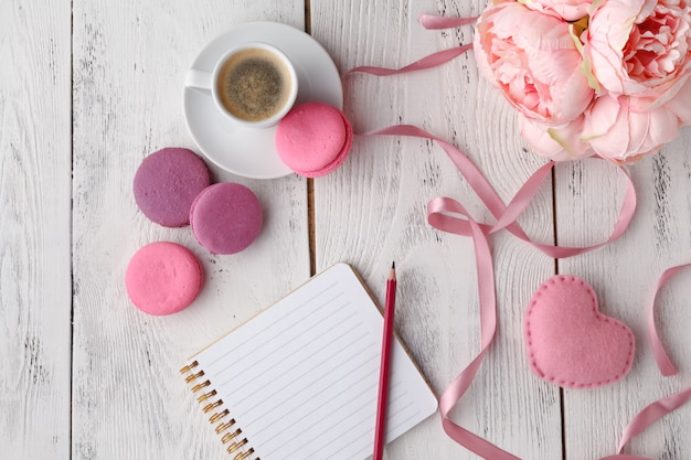 Photo macarons roses avec une tasse de café sur une table en bois. mise à plat