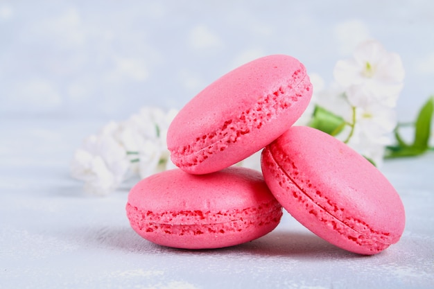 Macarons roses et violets sur une table grise entourée de fleurs roses et blanches.