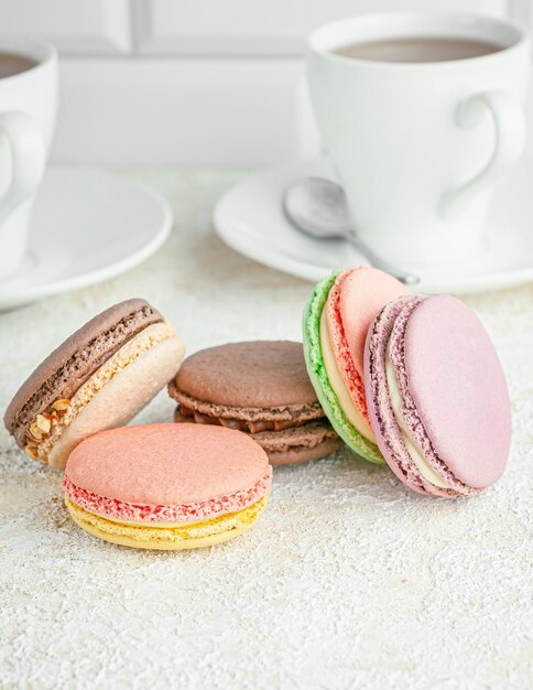 Des macarons sont disposés sur la table. Au fond, des tasses de café. Fermer. Fond clair.