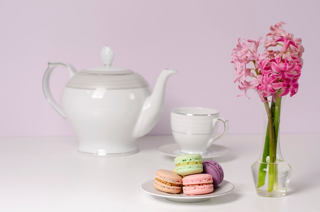 Macarons et vase transparent avec des fleurs de jacinthe rose sur une théière en porcelaine et une tasse