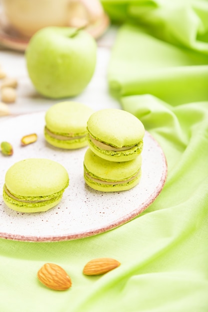 Macarons verts ou gâteaux macarons avec tasse de café sur une surface en bois blanc et textile en lin vert