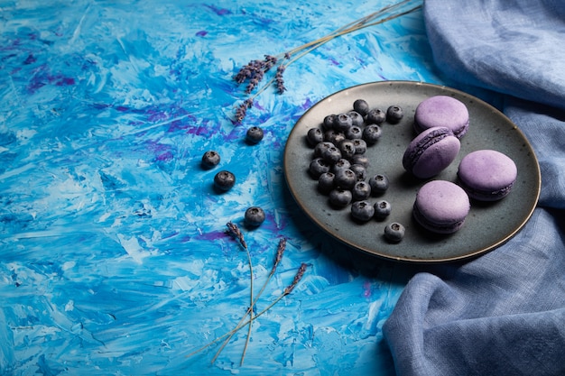 Macarons violets ou gâteaux macarons aux bleuets sur plaque en céramique sur un fond de béton bleu.