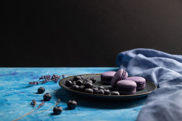 Macarons violets ou gâteaux macarons aux myrtilles sur plaque en céramique. Vue latérale, copiez l'espace.