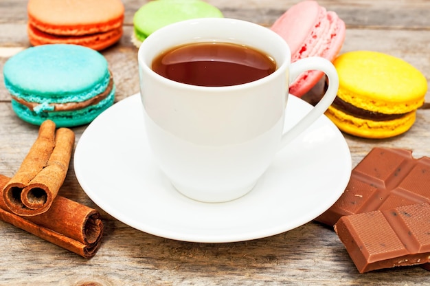 Macaroon avec du thé, du chocolat et des bâtons de cannelle sur une table en bois