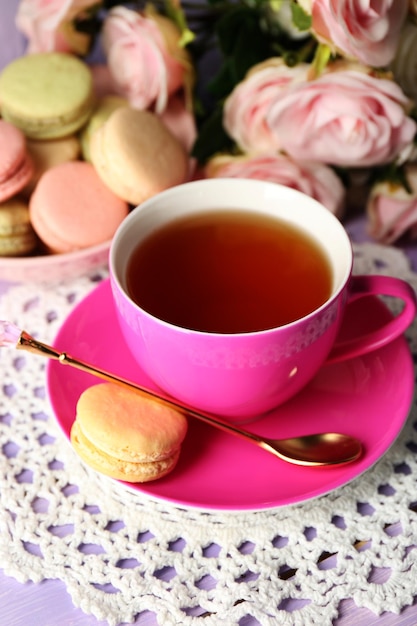 Des macaroons colorés avec une tasse de thé sur fond de bois