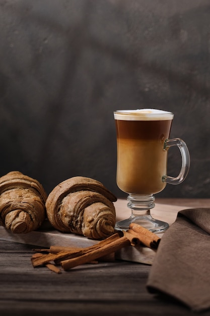 Macchiato tardif dans un grand verre sur un plateau en bois Tardif à la cannelle et croissants frais