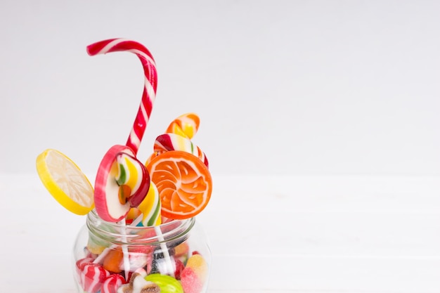 Mâcher des bonbons, des sucettes lumineuses avec de la canne en bonbon et des bonbons à la gelée dans la boîte en verre sur un tableau blanc en bois