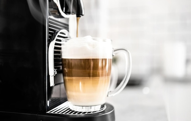 Machine à café avec capsules et cappuccino crémeux dans une tasse transparente à la maison expresso caféine beve
