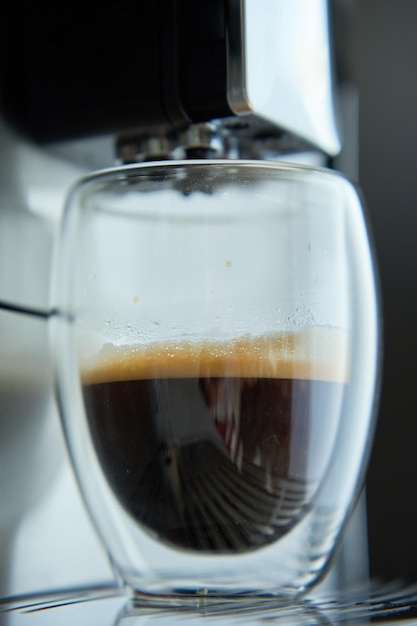 La machine à café prépare de l'espresso frais dans un verre clair sur un fond sombre