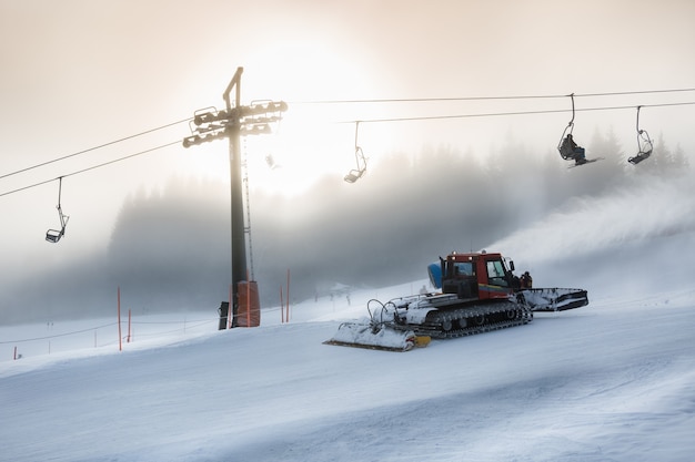 Machine de déneigement travaillant sur une pente de ski élevée à la tempête de neige