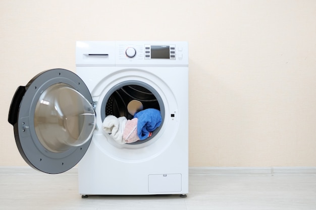 Machine à laver avec blanchisserie dans le tambour près du mur beige