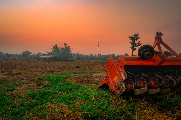 Machine de répression des crêtes. Fourniture pour tracteur. Machines agricoles dans la ferme agricole. Ferme de riz le matin avec un ciel de lever de soleil rouge. Nature des terres agricoles. Cabane d'agriculteur et poteau électrique dans les terres agricoles.