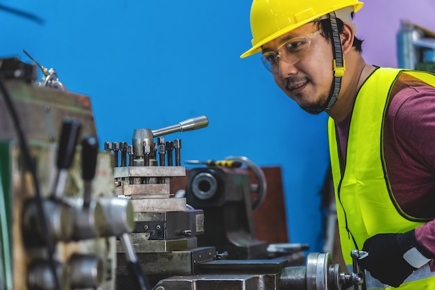 Machiniste asiatique en combinaison de sécurité, actionnant les tours professionnels dans une usine de travail des métaux