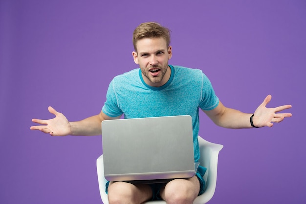 Macho en colère avec ordinateur portable sur fond violet. Homme en tshirt bleu avec ordinateur sur fond violet. Surfer sur Internet et monde virtuel. Blog ou blog et blog. La vie moderne dans le réseau social