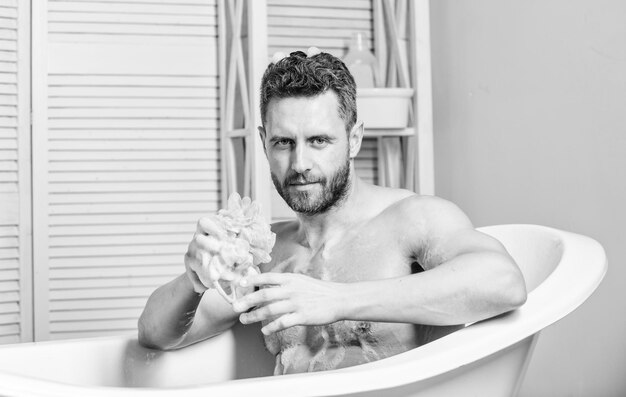 Macho avec une éponge prendre un bain à la maison Prendre un bain avec de la mousse de savon Routine de soins et de beauté Bel homme musclé Baignoire relaxante Concept de bain chaud Transformez votre salle de bain en propre spa privé