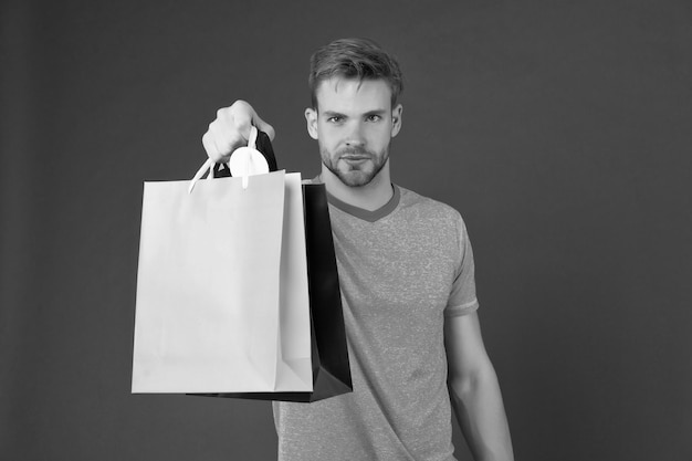 Macho avec des sacs en papier colorés sur fond violet Homme avec des sacs à provisions Shopper de mode en t-shirt bleu décontracté Préparation et célébration des fêtes Shopping ou vente et cyber lundi