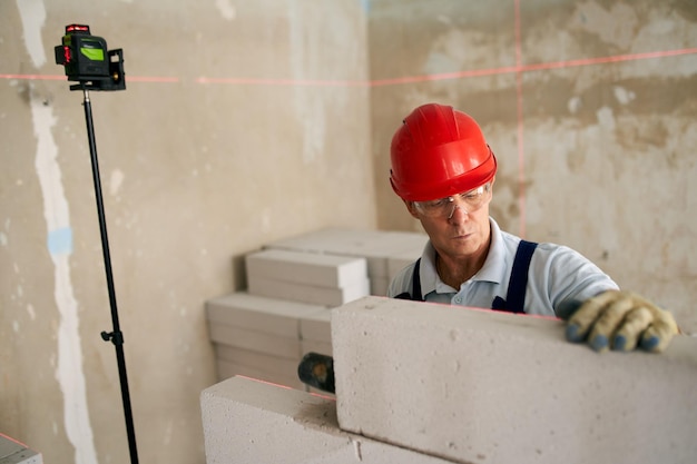 Maçon à l'aide d'un maillet en caoutchouc pour taper et niveler les blocs de béton. L'entrepreneur utilise des murs précis