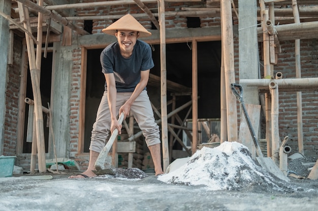 Maçon asiatique tenant une houe pour la pâte pour le sable et le ciment pour les bâtiments contre un fond de construction de maison