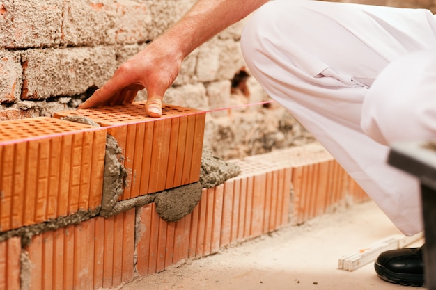 Maçon faisant le mur avec la brique et le coulis