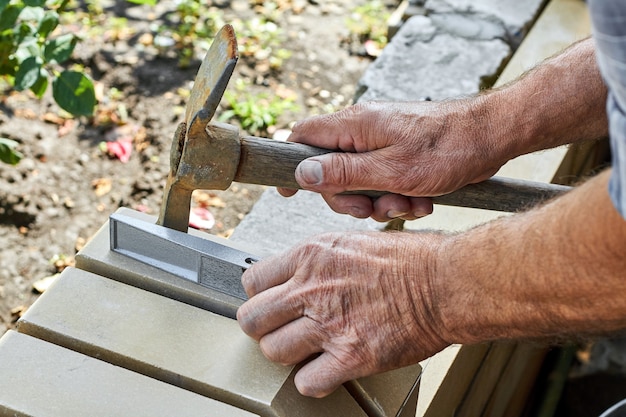 Maçon installant des briques sur la nouvelle clôture à partir de briques de parement à l'aide d'un marteau et d'un niveau de construction