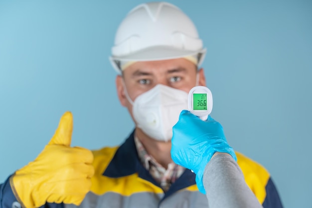 Un maçon, un ouvrier portant un masque de protection et un casque font mesurer leur température pour un dépistage de la grippe. Un homme sur fond bleu montre un geste de classe lors de la mesure de la température corporelle.