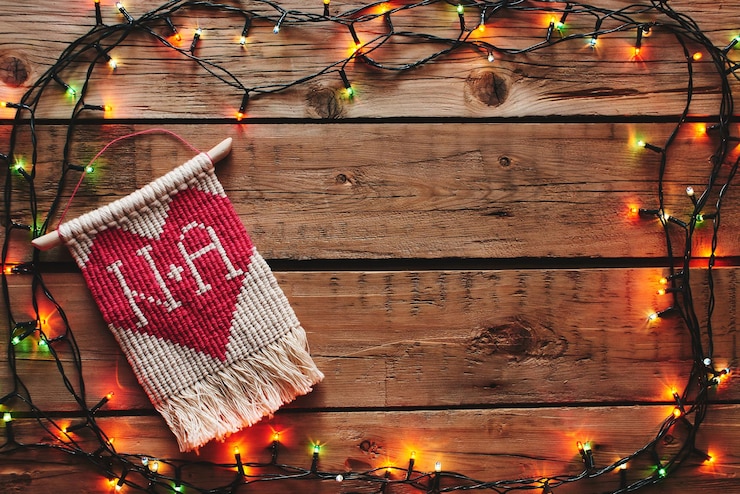 Photo macramé avec un coeur rouge encadré d'une guirlande de noël sur une table en bois. un cadeau pour la saint-valentin.
