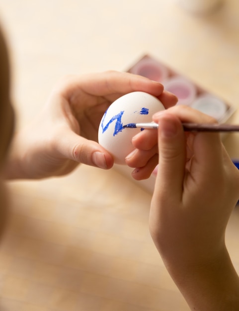 Macro photo d'enfant peignant l'oeuf de Pâques avec la brosse
