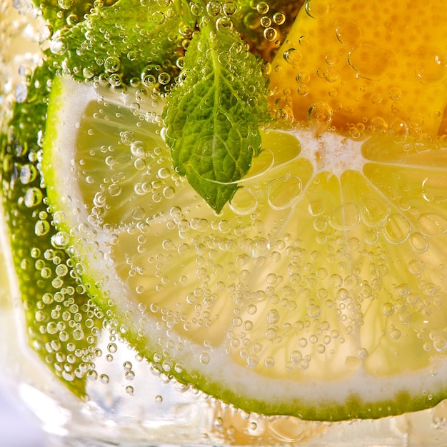 Macro photo de tranches fraîches de citron vert, de citron jaune et de feuille de menthe avec des bulles dans un verre. Cocktail rafraîchissant d'été