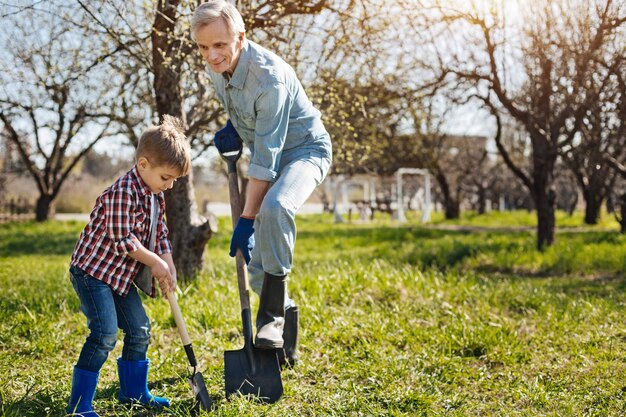 Magnifique activité familiale. Grand-père portant des gants de jardin bleu marine passer du temps libre avec son petit-enfant à l'extérieur tout en jardinant ensemble