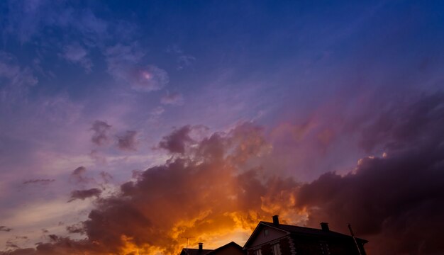 Un magnifique coucher de soleil rouge, orange et rose sur un ciel nuageux et des silhouettes de toits de maisons.