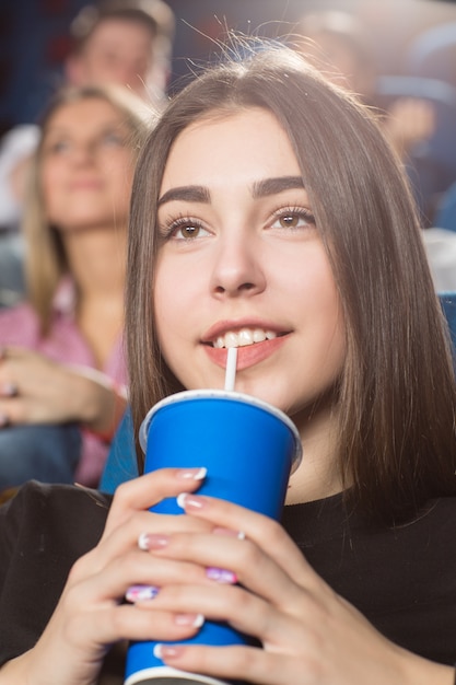 magnifique femme brune à boire en regardant des films au cinéma souriant joyeusement