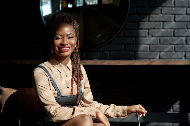 Une magnifique femme noire souriante dans les murs sombres, la lumière du soleil à l'intérieur de la pièce, portrait d'un conseiller consultant.