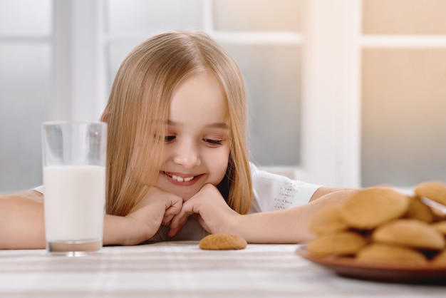 Magnifique petite fille avec de beaux cheveux de sourire se trouve près des cookies