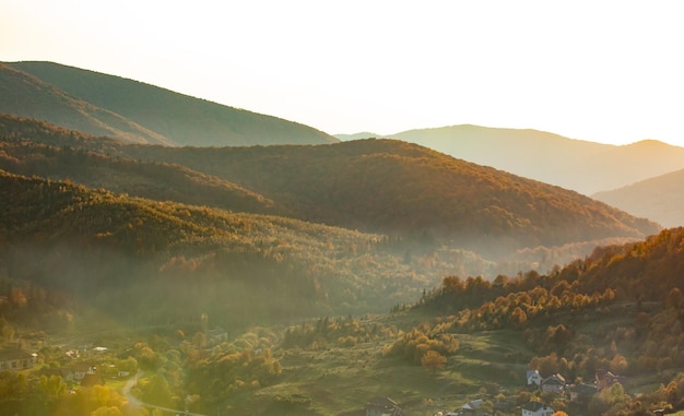 Magnifique scène de lever de soleil dans le paysage de montagnes avec des poutres ensoleillées Le village est situé dans la vallée et est recouvert d'un léger brouillard matinal