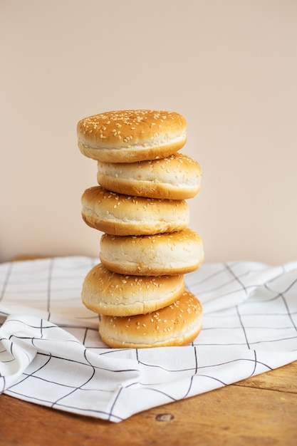 De magnifiques petits pains fraîchement cuits pour les hamburgers se trouvent l'un sur l'autre sous la forme d'une tour sur une table en bois avec une serviette à carreaux blancs