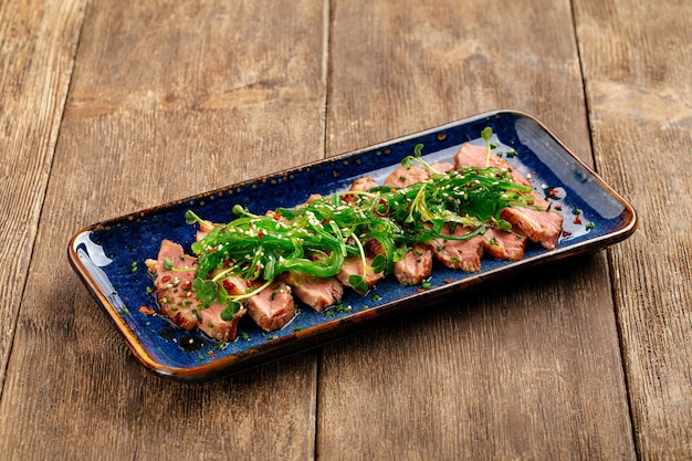 Photo magret de canard rôti tataki en tranches avec chuka d'algues sur le fond en bois