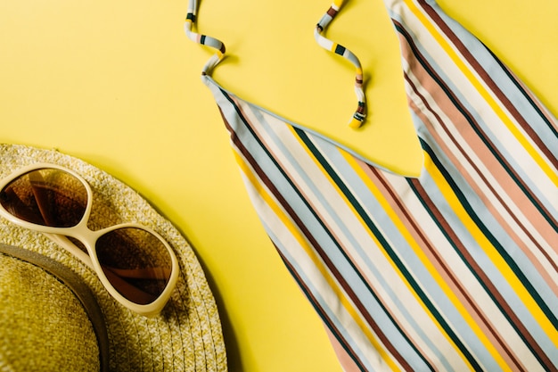 Maillot de bain rayé, lunettes de soleil, chapeau de paille sur fond jaune, pose à plat. Accessoires de plage pour femmes. Fond d'été. Concept de voyage. vue de dessus. Photo de haute qualité