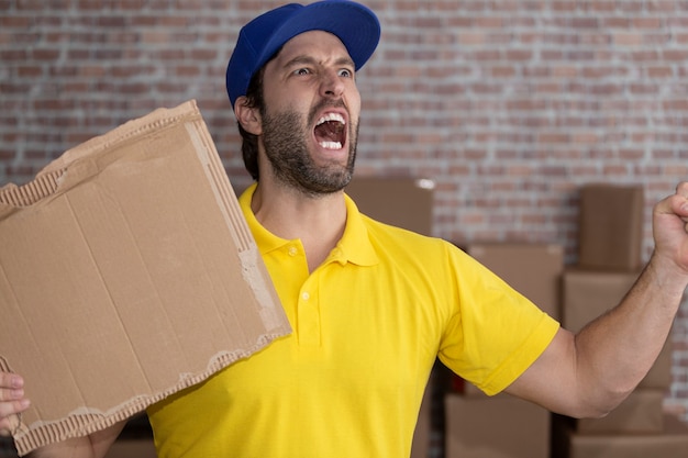 Mailman brésilien tenant un tableau vierge dans un dépôt avec beaucoup de boîtes. Copiez l'espace.