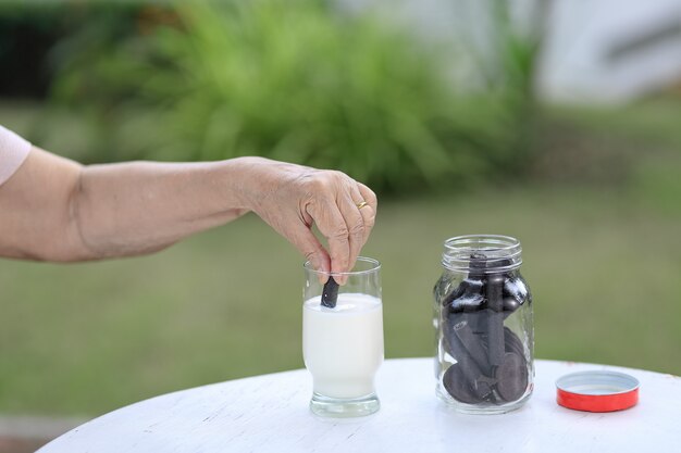 Main âgée trempant un biscuit au chocolat dans un verre de lait