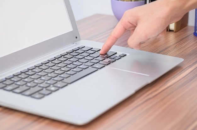 Main à l'aide d'un ordinateur portable au bureau dans la chambre