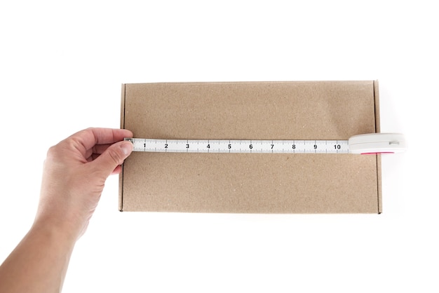 La main à l'aide d'un ruban à mesurer mesure une boîte en carton contre une surface blanche. Taille de boîte.