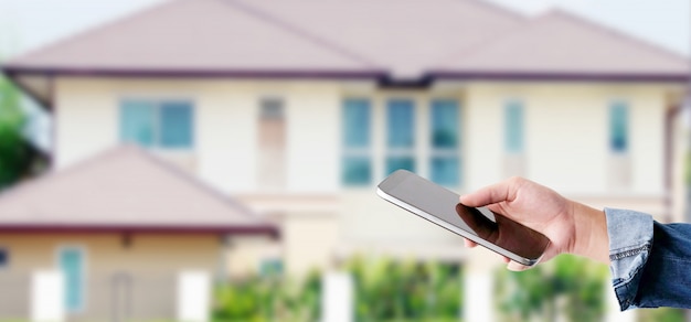 Main à l&#39;aide de téléphone intelligent sur fond de maison flou