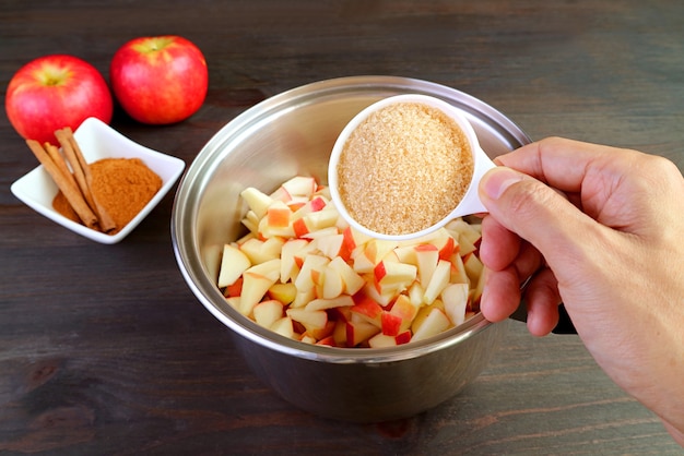 Main en ajoutant une tasse de sucre non raffiné dans le pot de pommes fraîches en dés pour faire de la compote de pommes