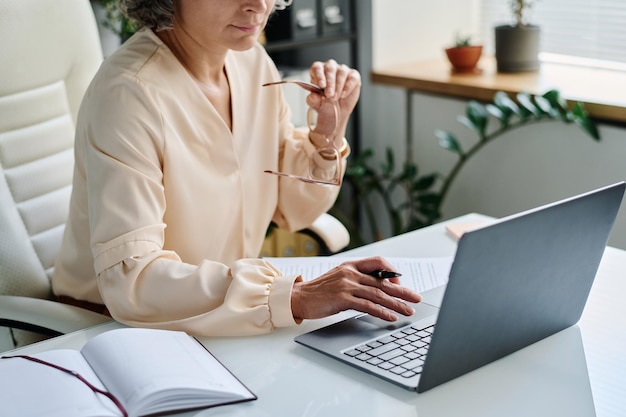Main d'une analyste féminine mature sur un clavier d'ordinateur portable pendant le réseau